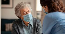Foto que muestra a una persona mayor con mascarilla siendo visitada por una trabajadora de la salud