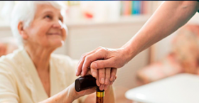 Una persona mayor sonrie mirando hacia arriba mientras una funcionaria de salud posa su mano sobre la suya