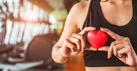 Foto de una mujer con ropa deportiva sosteniendo una figura de corazon entre sus dedos