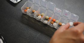 Foto que muestra las manos de una persona organizando medicamentos en un pastillero